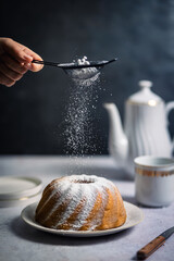 Eine Frau streut Puderzucker &uuml;ber einen Gugelhupf. Dessert, stillleben.