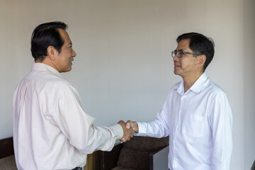 Two successful Asian businessmen shaking hands in agreement during a professional meeting. Partnership, deal, and teamwork concept on a modern textured background.