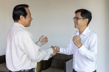 Two happy successful Asian businessmen shaking hands in agreement during a professional meeting. Partnership, deal, and teamwork concept on a modern textured background.