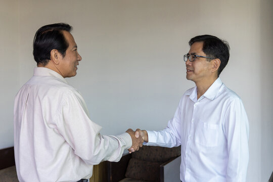 Two successful Asian businessmen shaking hands in agreement during a professional meeting. Partnership, deal, and teamwork concept on a modern textured background.