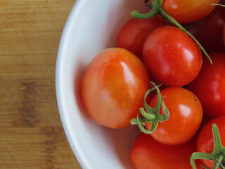 Closeup of bowl of small red tomatoes on wooden surface. Tomatoes in a bowl.