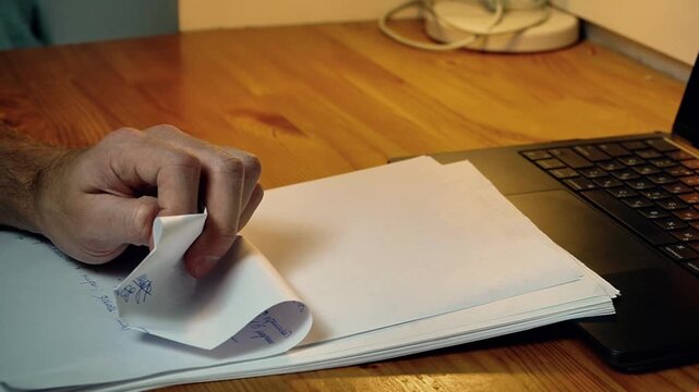 Close-up hands crumpling sheet of paper in frustration failed attempt creative block dissatisfaction with work sitting at desk evening warm light home office stress moment