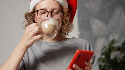 Smiling woman in Santa hat shopping online smartphone for Christmas gifts while drinking coffee, enjoying festive season and cozy home moments - Powered by Adobe