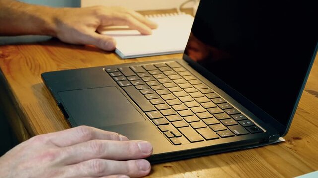 Close-up hands pushing laptop aside and pulling spiral notebook closer reorganizing workspace switching from digital to analog notes home office creative work evening warm light
