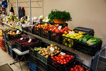 Crates of apples, tomatoes, onions, herbs, cranberries, and other fresh fruits and vegetables arranged on display at a vibrant indoor market stall