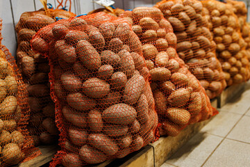 Large sacks of potatoes stored in red mesh bags, stacked on wooden pallets indoors at a wholesale or market facility