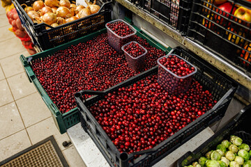 Bulk fresh cranberries displayed in black and green crates, with several plastic containers filled for individual sale at an indoor market stall
