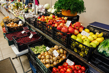 Obraz premium Crates of apples, tomatoes, onions, herbs, cranberries, and other fresh fruits and vegetables arranged on display at a vibrant indoor market stall