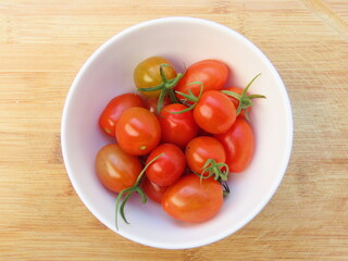Closeup of bowl of small red tomatoes on wooden surface. Tomatoes in a bowl.