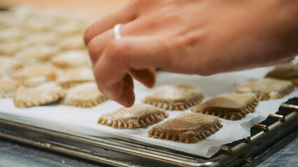 Hand placing uncooked fresh ravioli pasta onto a baking tray, preparing traditional Italian food for cooking, capturing a culinary art and craftsmanship concept