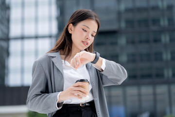 Young asian businesswoman in city talking to smartwatch using voice command with AI, professional business woman using artificial intelligence with watch, virtual assistant.