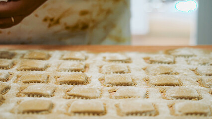 Artisan hands skillfully preparing fresh Italian ravioli from dough on a floured surface, creating traditional square pasta elements for a gourmet meal