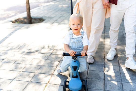 Happy toddler riding tricycle with parents walking outdoors