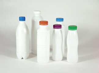 Six white plastic bottles with colorful screw caps (blue, orange, purple, green, and white) arranged in a group on a white background, representing beverage or dairy packaging.