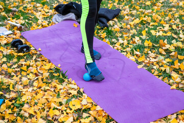 Person massaging foot with spiky ball outdoors on yoga mat