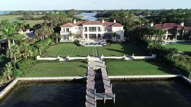 Aerial view of a luxury waterfront mansion with a dock on a sunny day. Real estate usage