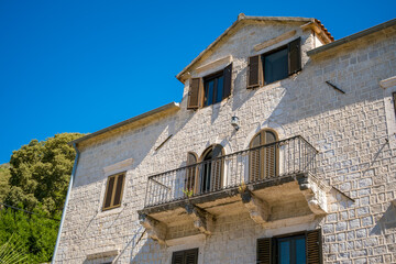 Historic stone building with a balcony in Perast, Montenegro. Clear blue sky in the background. Architectural details highlight the town's charm.