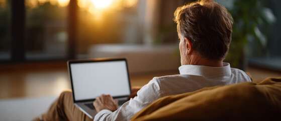 Middle-aged man working on laptop at home during sunset with warm natural light and cozy indoor setting