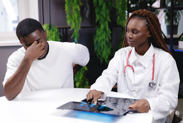 African male patient consults with female doctor analyzing x-ray in medical office setting. Help with back injuries, hernias and spinal protrusions.