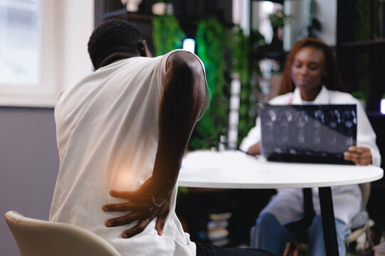 African male experiencing back pain during medical consultation with female doctor analyzing x-ray of spinal