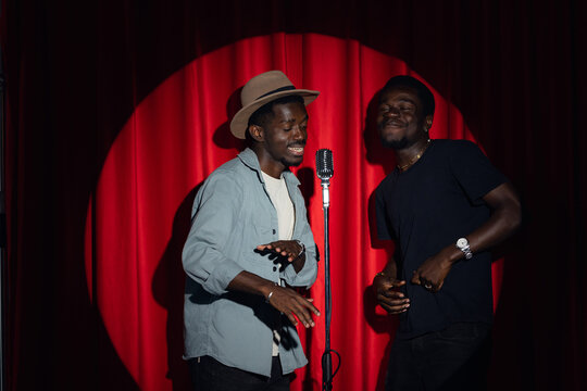 Professional jazz band, two african american mans pop music singer is performing song with retro microphone on stage with red curtains