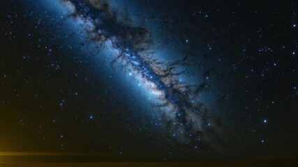 Stunning view of a swirling galaxy against a dark night sky featuring vibrant blue hues and sparkling stars captured from a wide perspective with faint warm light in the foreground.