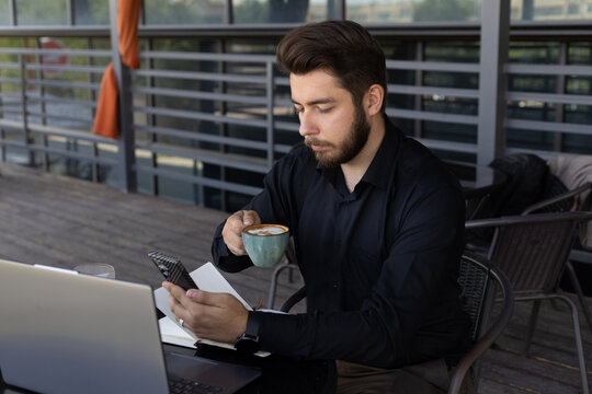 A man is drinking from a mug while using his smartphone.