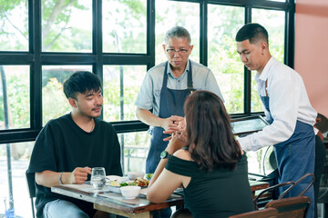 Elderly asian restaurant owner and waiter serving food to couple at table inside cafe teamwork hospitality communication cooperation small business management partnership friendly customer service