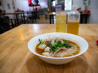 Thai Tom Yum Glass Noodle Soup with Pork Fishballs and Fresh Herbs in White Bowl