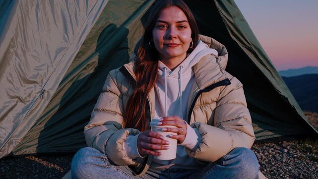 Serene camper enjoying warm beverage at sunset, framed by tent, capturing tranquil moment in nature, camera gradually zooms in to emphasize peaceful ambiance and connection with surroundings
