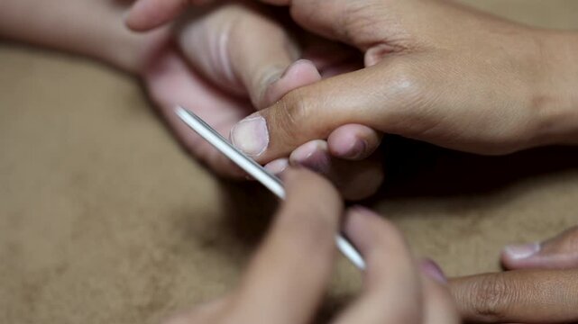 Close up of manicurist using nail file and buffer to shape and smooth fingernail in beauty salon for nail care concept.