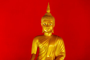 Fototapeta premium Selective focus of golden yellow image of Buddha with red wall as background, Close up Buddhist statue in public area allowed zone in the Thai temple, Religion and symbolism of buddhism, Thailand.