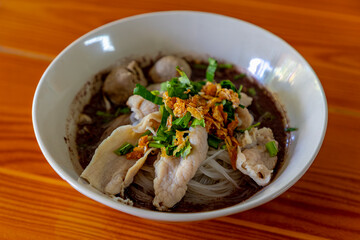 Selective focus of vegetable noodle with stewed pork soup with meatballs, Served in ceramic plastic bowl on the table, Delicious and favorite street food in Thailand.