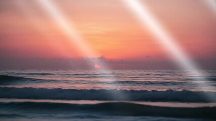 Sun setting over calm ocean waters with soft waves reflecting warm orange and pink hues beams of light streaming through clouds in a serene beach landscape at twilight