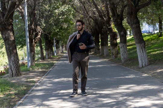 A man walking on a sidewalk, holding a cell phone - Powered by Adobe