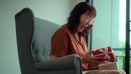 Happy pretty senior asian woman exciting while opening surprised a red gift box with joyful holiday celebration, healthy aging retirement lifestyle gratitude love and festive happiness concept.
