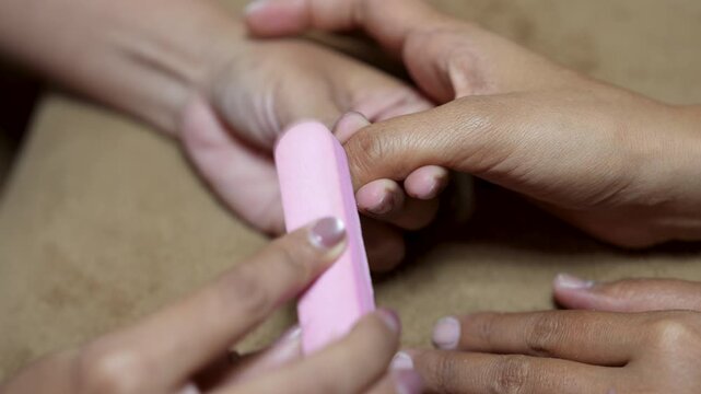 Close up of manicurist using nail file and buffer to shape and smooth fingernail in beauty salon for nail care concept.