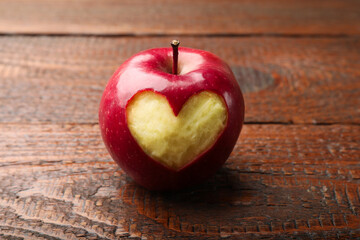 Ripe apple with carved heart on wooden table, closeup