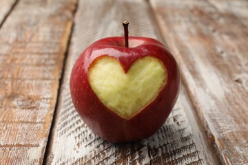Ripe apple with carved heart on color wooden table, closeup