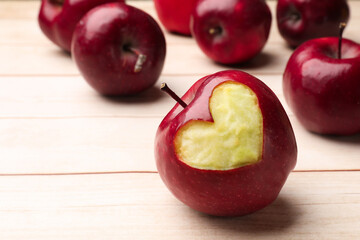Ripe apple with carved heart and whole ones on light wooden table, closeup