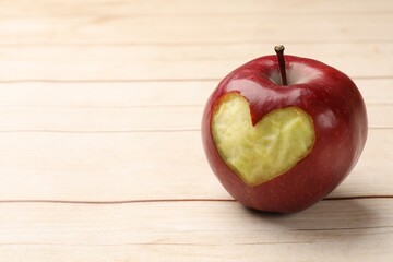 Ripe apple with carved heart on light wooden table, closeup. Space for text