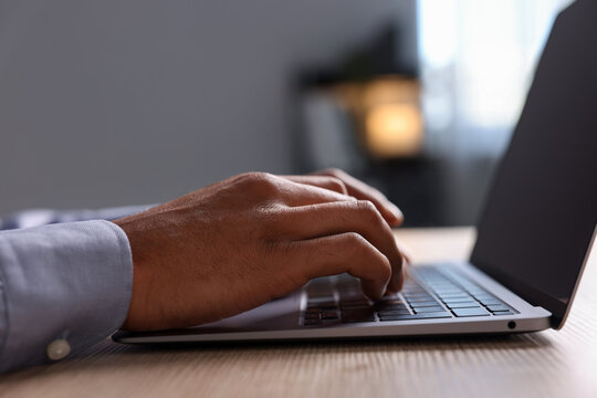 African-american man using laptop at wooden table indoors, closeup