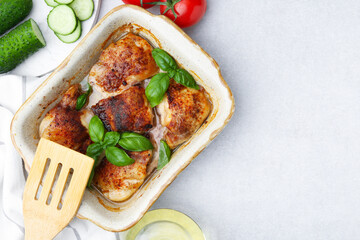 Tasty cooked chicken thighs with basil in baking dish and ingredients on light grey table, flat...