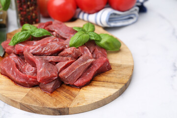 Pieces of raw beef meat, basil and ingredients on white marble table, closeup. Space for text