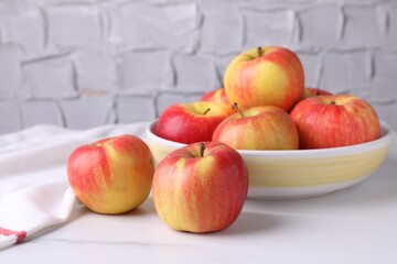 Ripe red apples and bowl on white table near grey textured wall, closeup