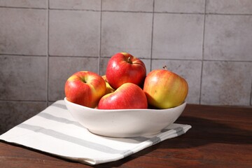 Ripe red apples in bowl on wooden table near grey tiled wall, closeup
