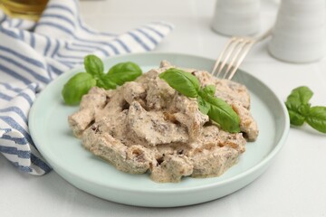 Tasty beef Stroganoff with basil on white table, closeup