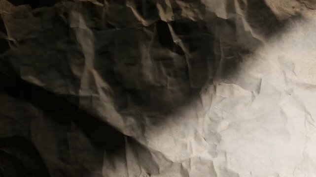 Textured crumpled paper background shifting between light and shadow with smooth transitions highlighting subtle details and variations in color and depth over time.