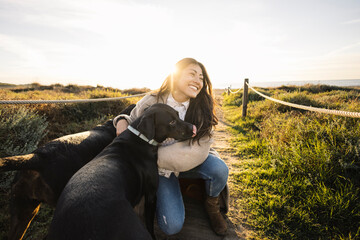 Woman petting black dog during sunset walk on beach path