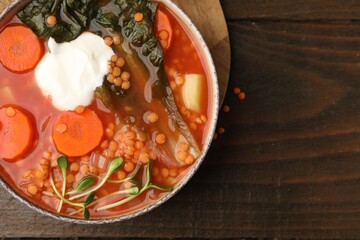 Tasty lentil soup with sour cream and vegetables in bowl on wooden table, top view. Space for text
